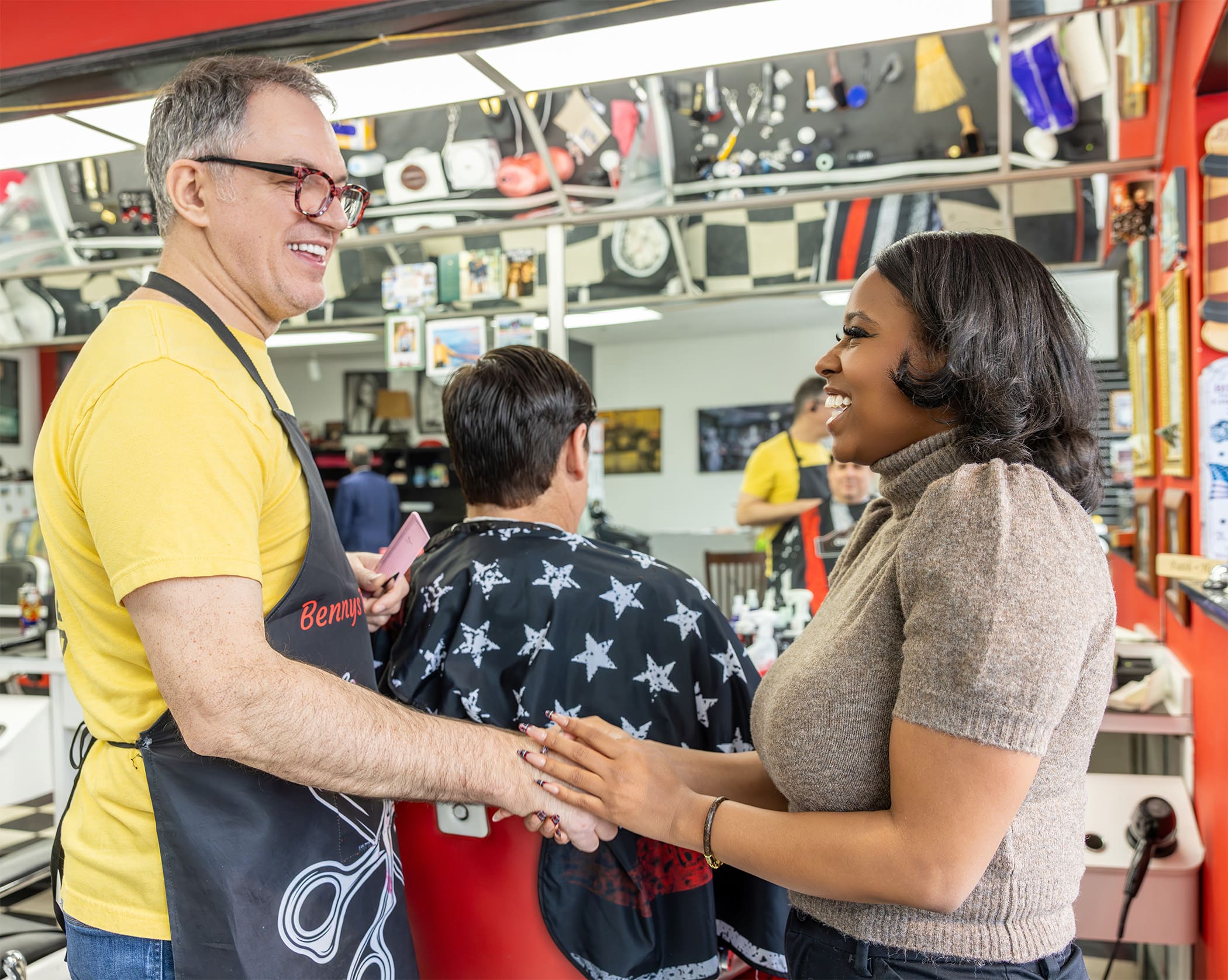 Shantel Franklin sharking hands with a smiling barber at Benny's Barber Shop. The barber is a white man holding a comb and wearing a navy apron that says "Benny's"
